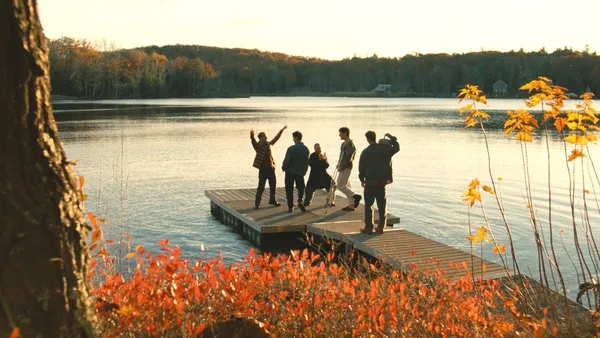 A still from the film Before I Do. It's Autumn, and five men stand on a wooden jetty which stretches out into a lake surrounded by forest.