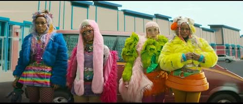 A still from the film I Love Boosters. Four Black women in elaborate, brightly coloured clothes and hair accessories stand in a car park.